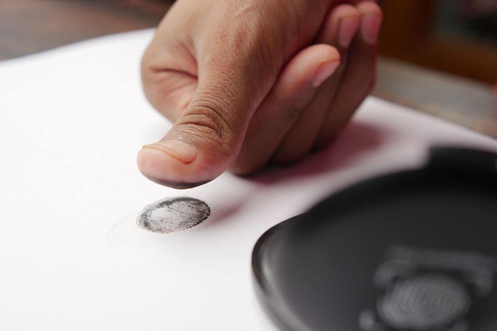 A thumb pressing an inked fingerprint onto white paper