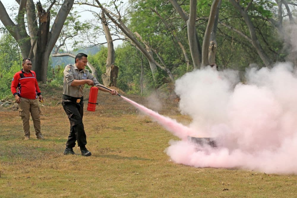 A uniformed officer practising with a fire extinguisher while an instructor watches during outdoor safety training