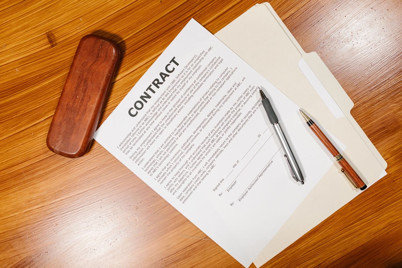 A printed contract and two pens beside a wooden pen case on a desk