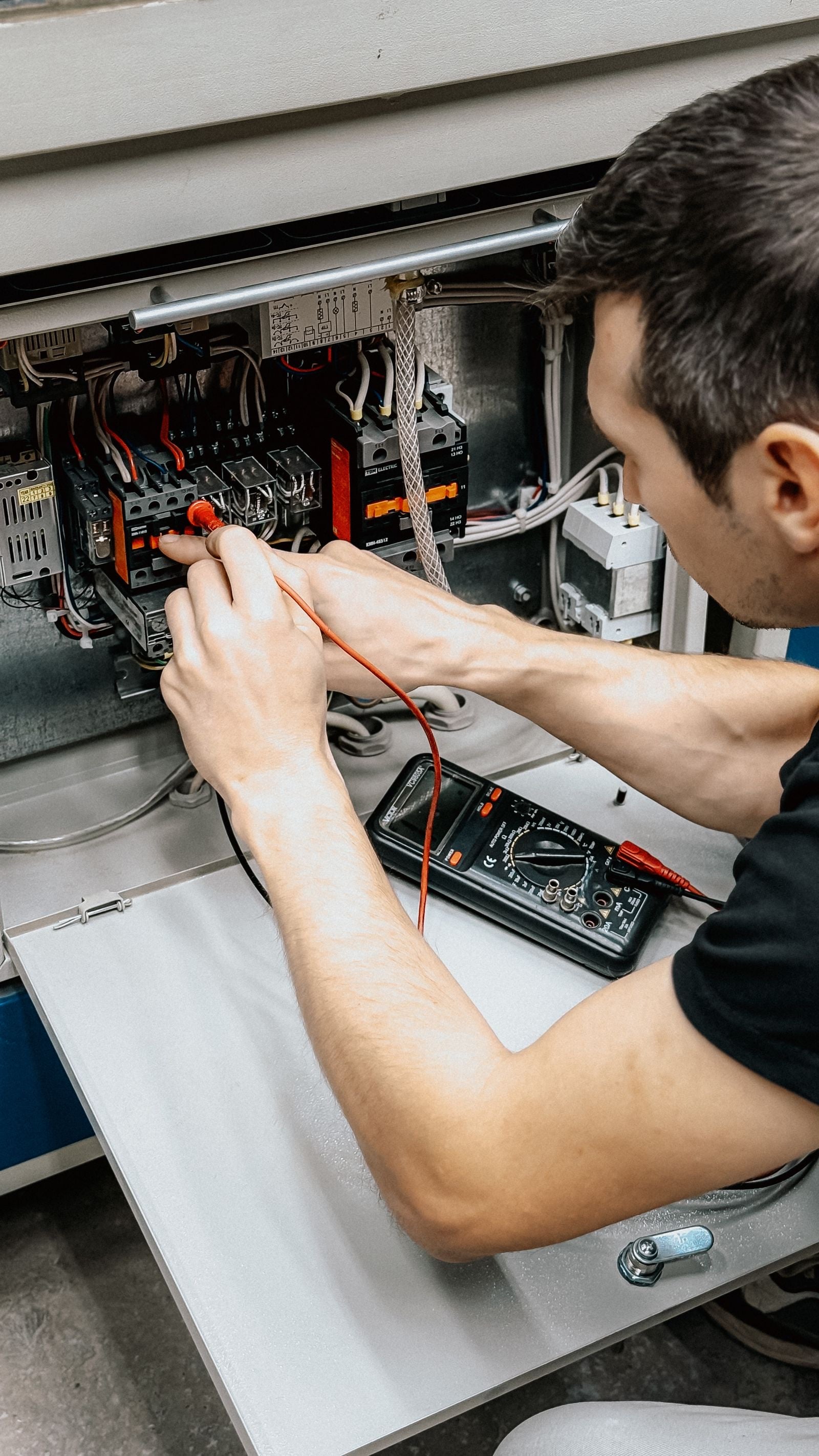 An electrician tests the wiring inside an open control panel with a multimeter