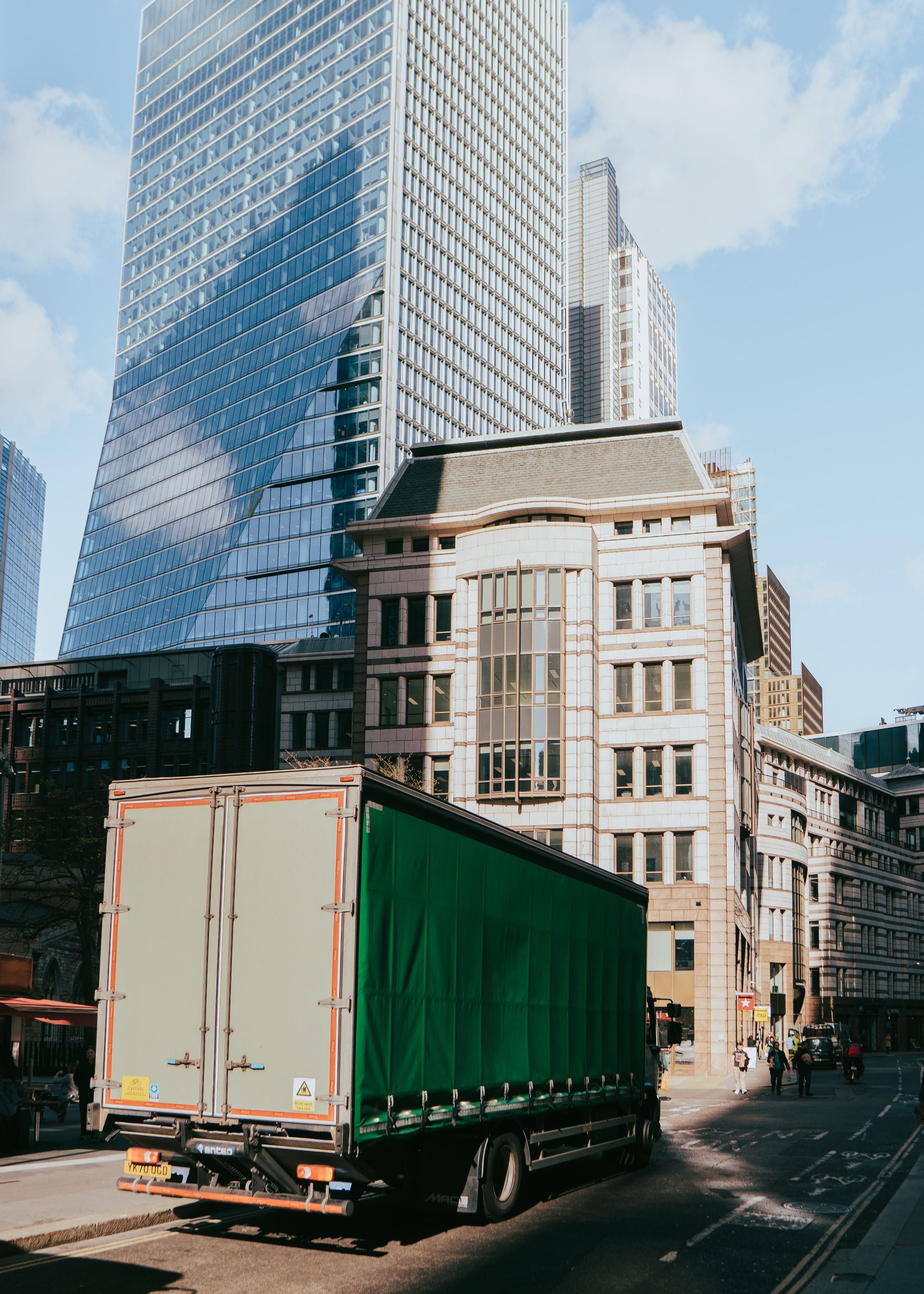 A rigid curtainsider lorry turns into a street in the City of London beneath the 100 Bishopsgate tower