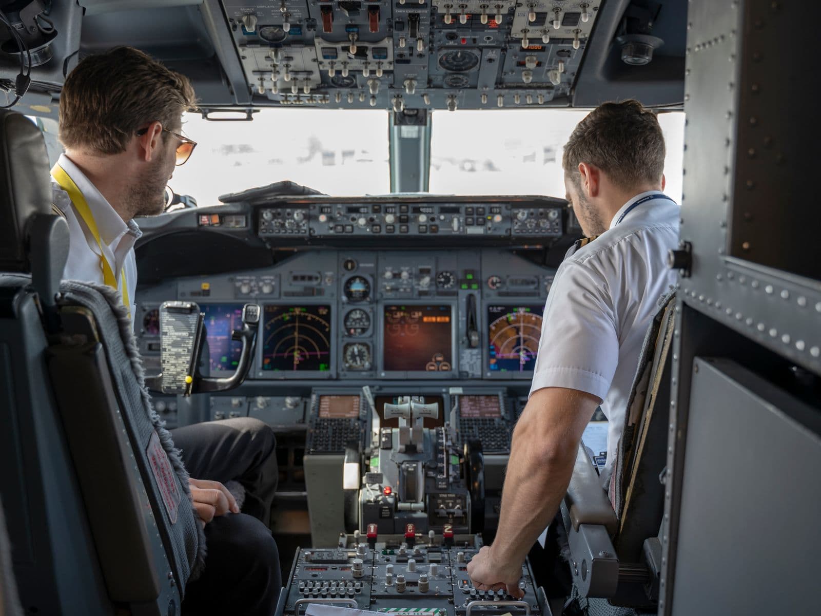 A captain and a first officer in white shirts work together in an airliner cockpit