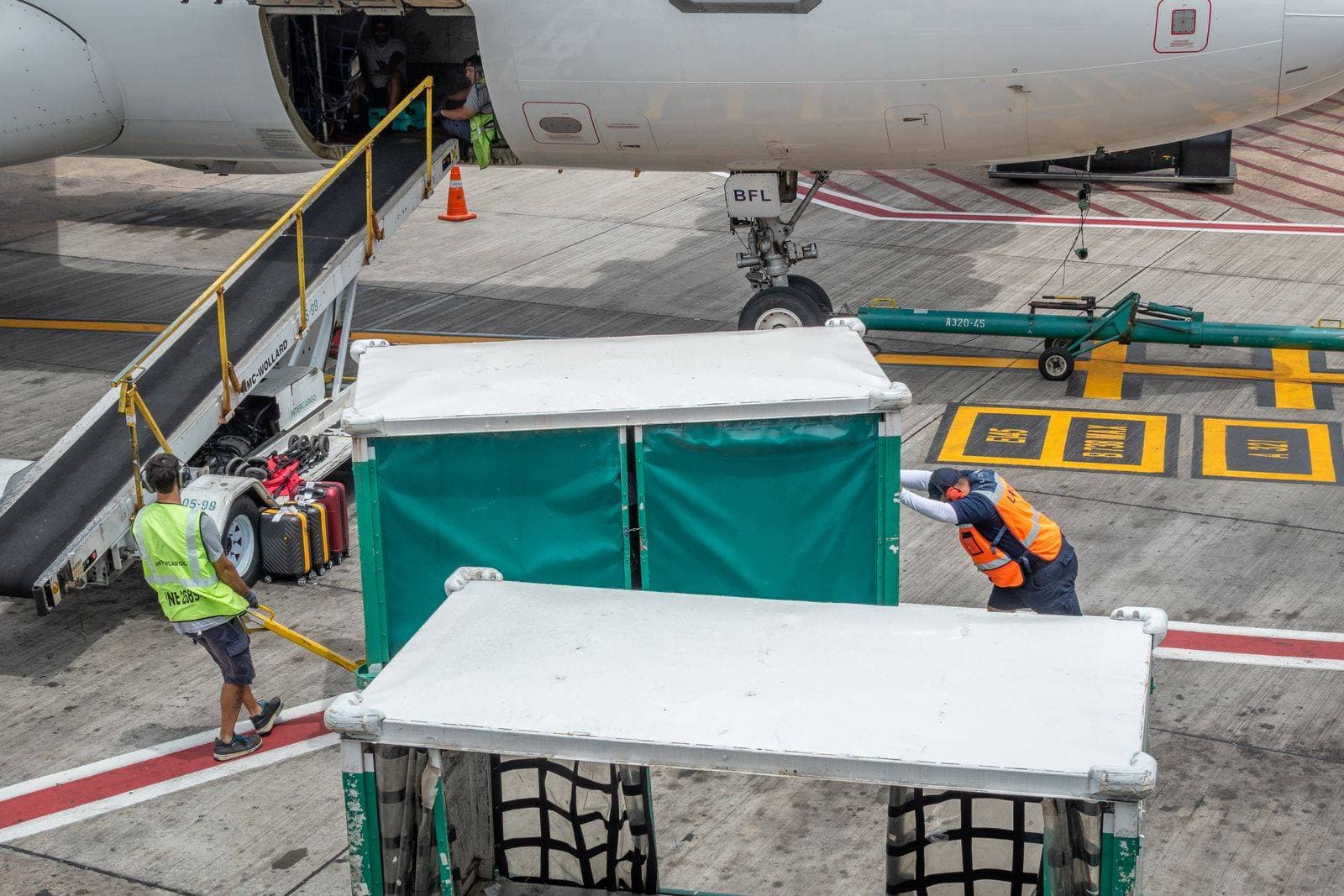 Ground crew in hi-vis vests load baggage carts beside a belt loader at an aircraft’s hold