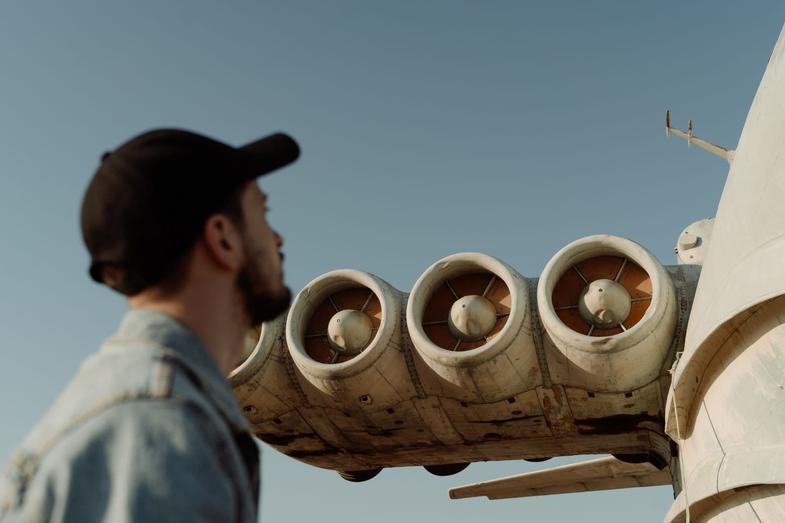 A man in a cap looks up at the rear engines of a parked jet