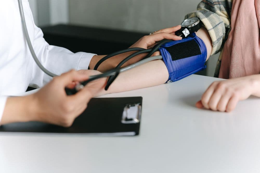 A medical examiner takes a patient’s blood pressure with a cuff at a desk