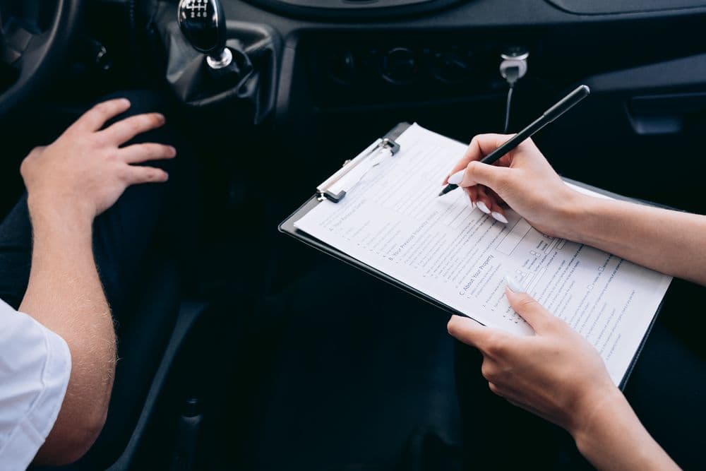 Hands filling in a form on a clipboard in the driver’s seat of a vehicle