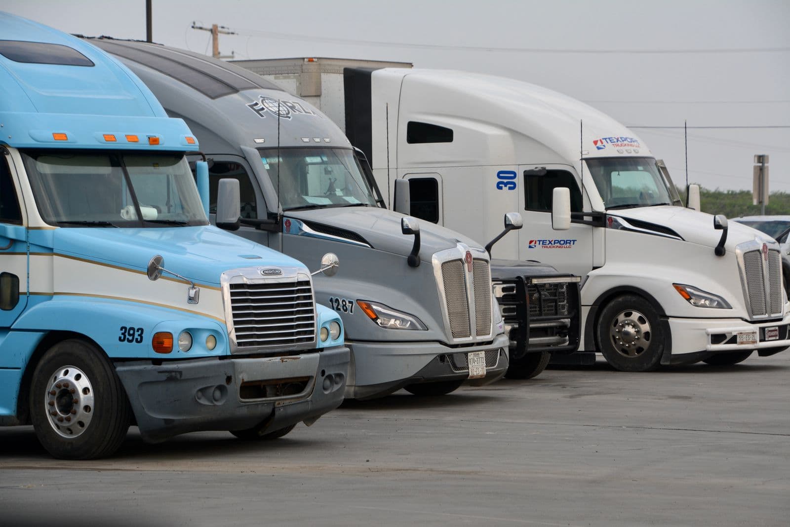 A row of long-nose semi-truck tractors parked side by side at a truck yard in Texas