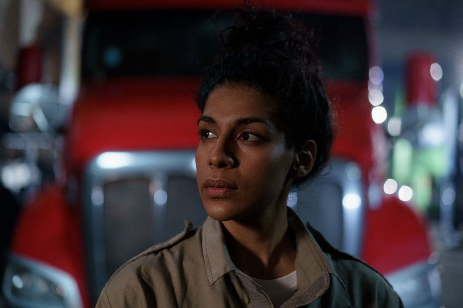 A driver in a work shirt waits with a worried look in front of a red semi-truck at night