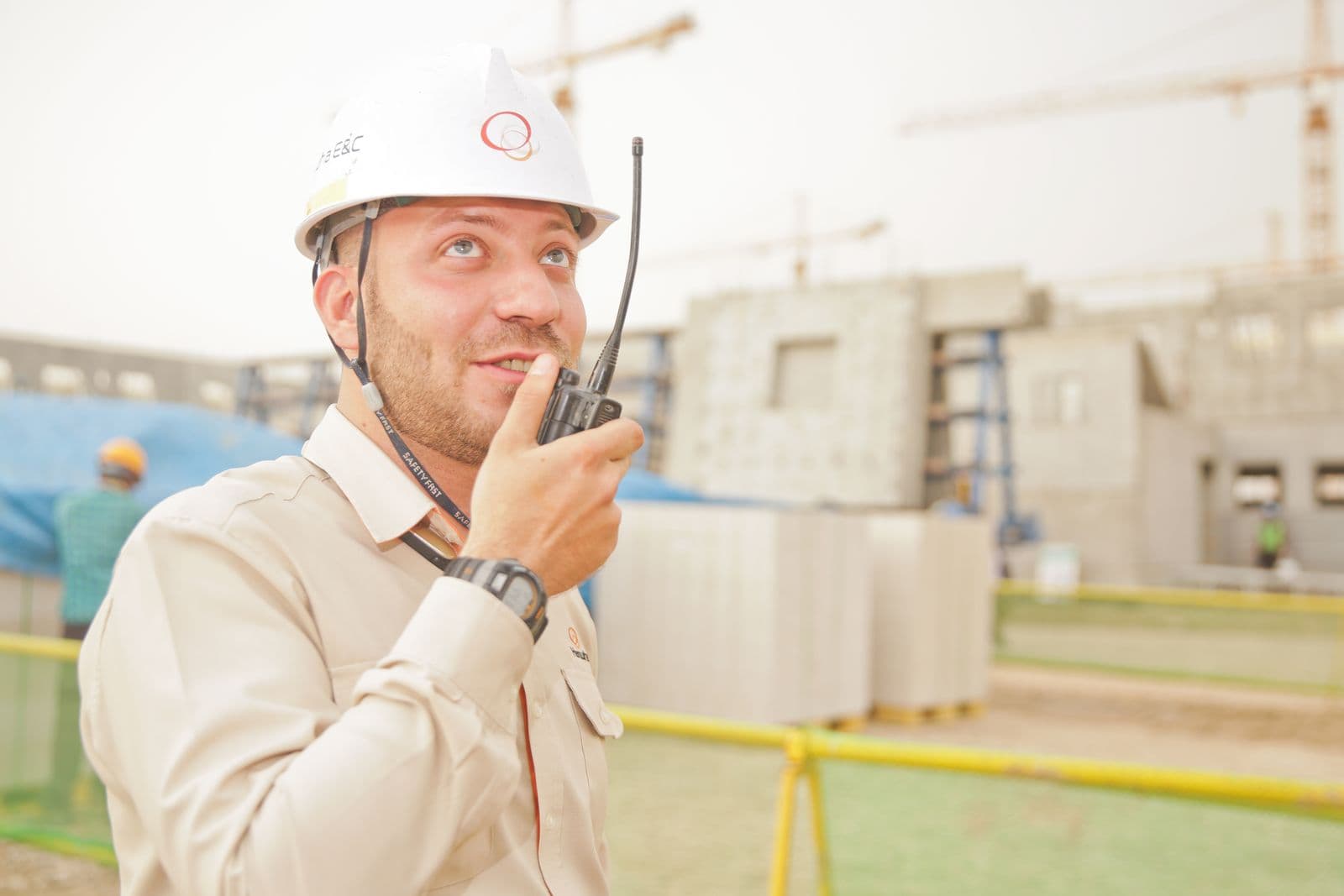 A site supervisor in a hard hat talking into a radio at a construction site