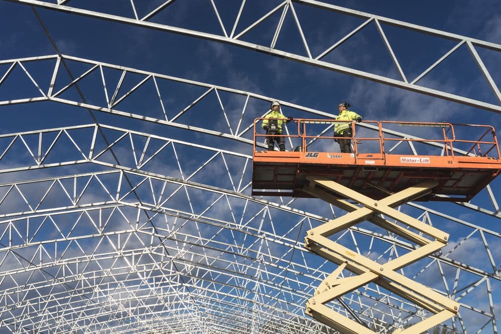 Two workers on a scissor lift beneath a steel roof frame