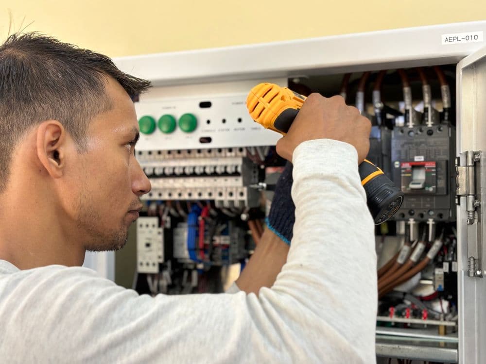 An electrician using a drill inside an open electrical panel