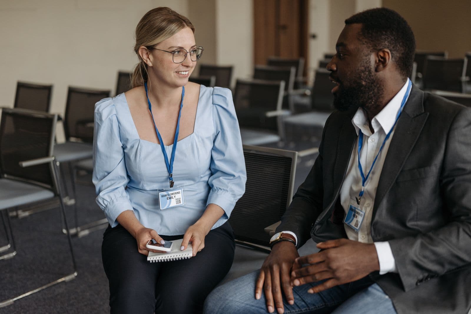 Two colleagues wearing ID badges on lanyards talking and smiling in a training room