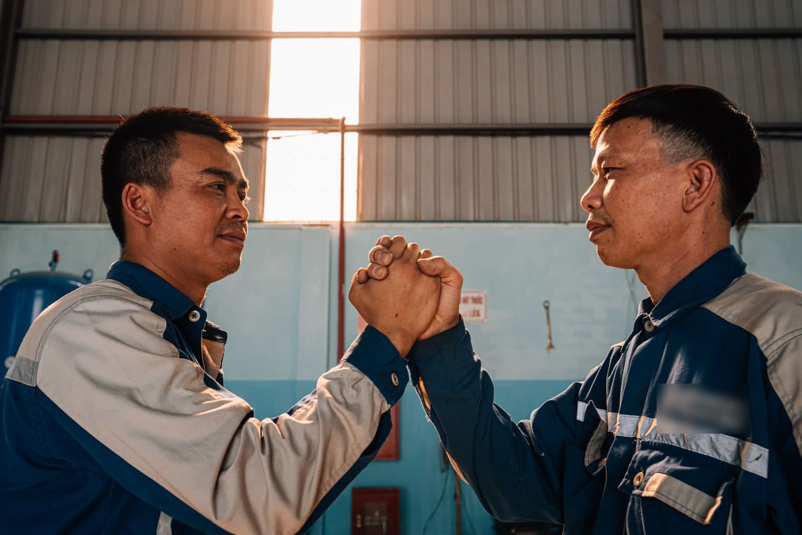 Two workshop technicians in work jackets clasp hands and smile at each other