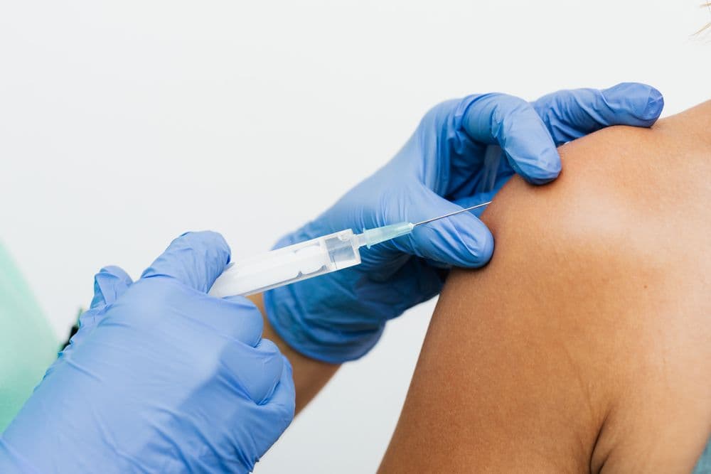 A gloved clinician giving a vaccination in the upper arm
