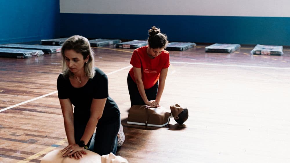 Two women practicing chest compressions on CPR training manikins in a gym