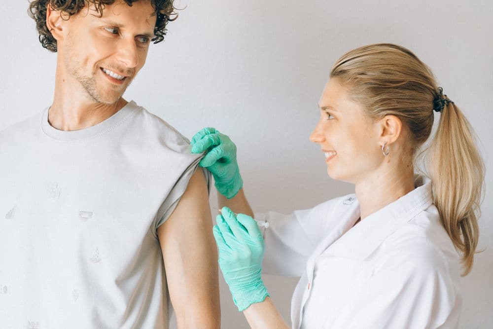 A nurse in green gloves giving a smiling man a vaccination in the upper arm