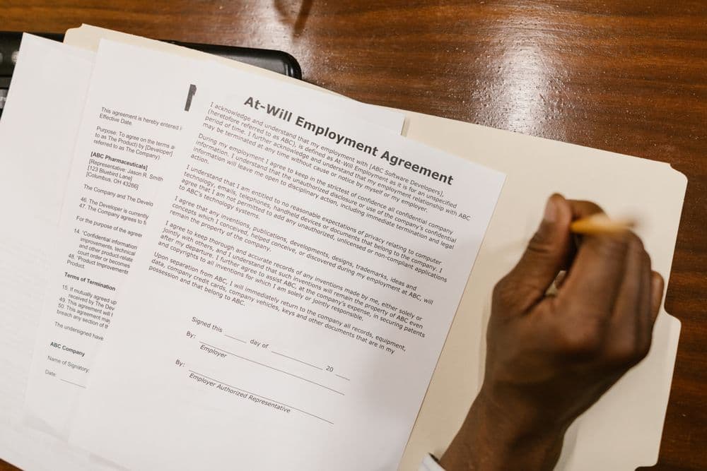 A hand signing an at-will employment agreement on a wooden desk