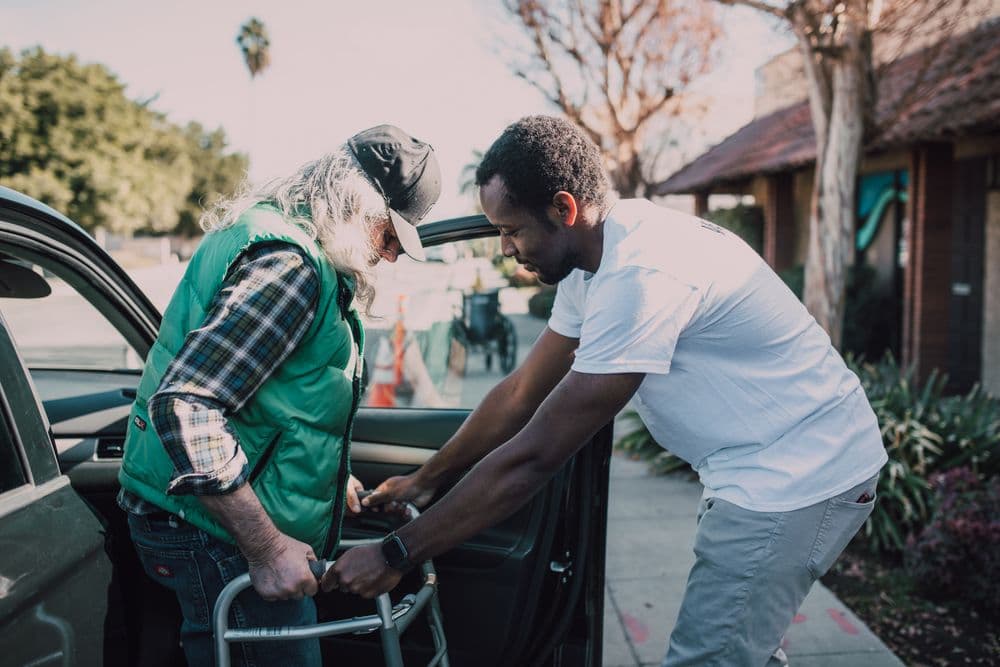 A young man helping an older man with a walker out of a parked car