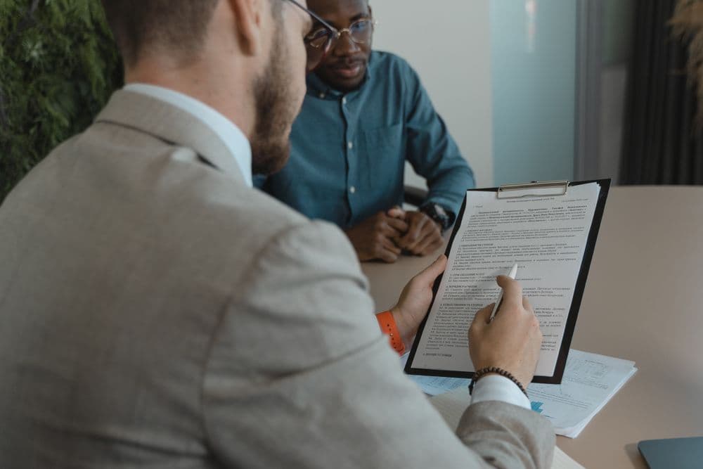 A recruiter at a table reviewing a candidate’s paperwork on a clipboard while the candidate waits