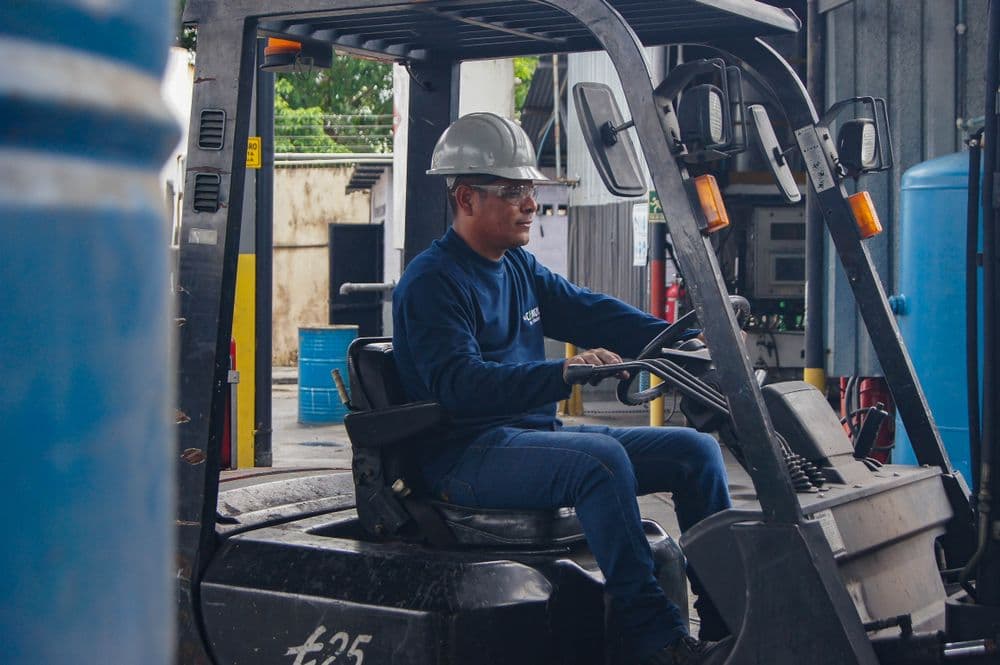 A forklift operator in a hard hat driving inside an industrial building