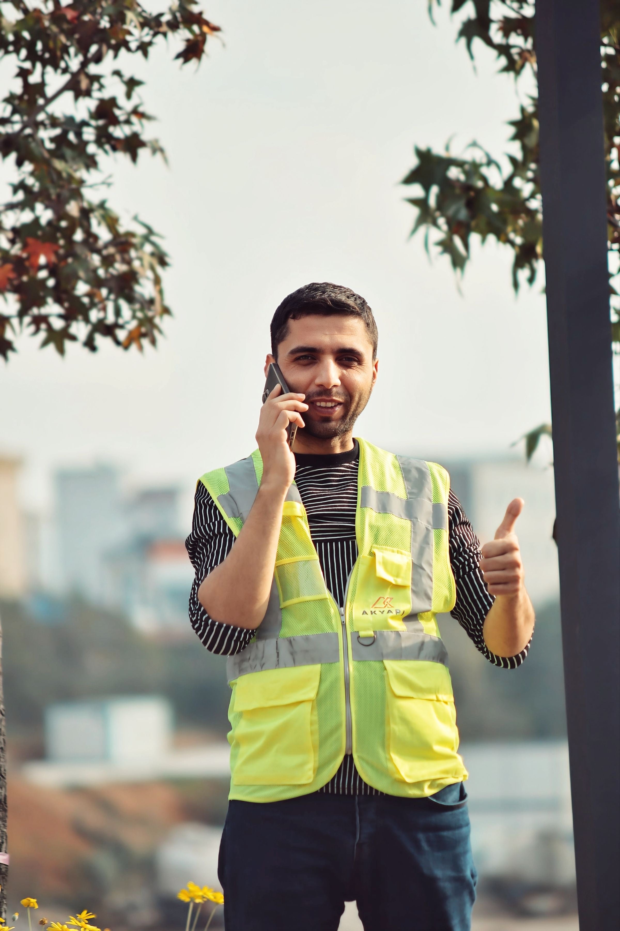 A smiling worker in a yellow hi-vis vest on the phone, giving a thumbs up
