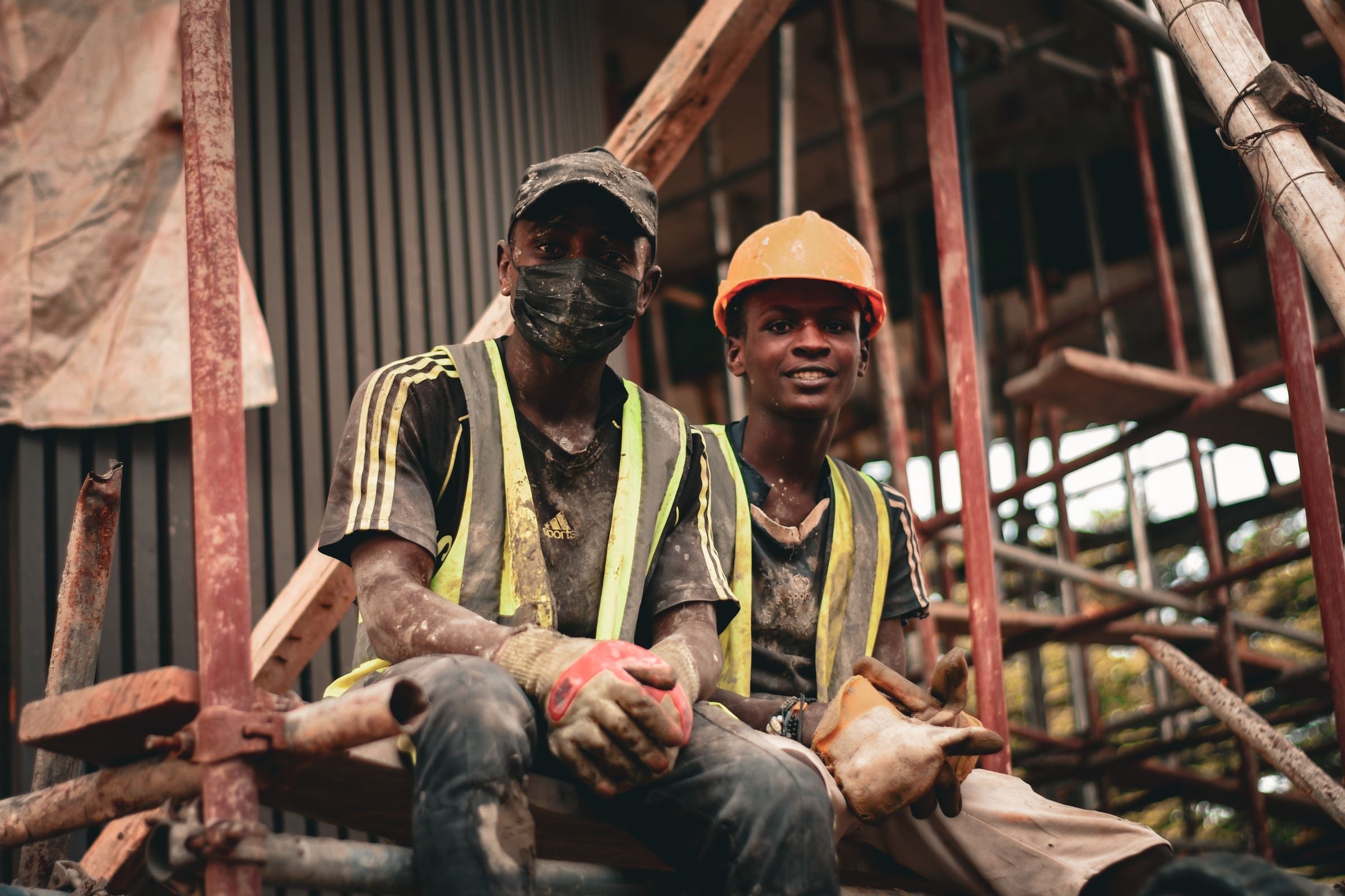 Two operatives in hi-vis vests and work gloves taking a break on a scaffold