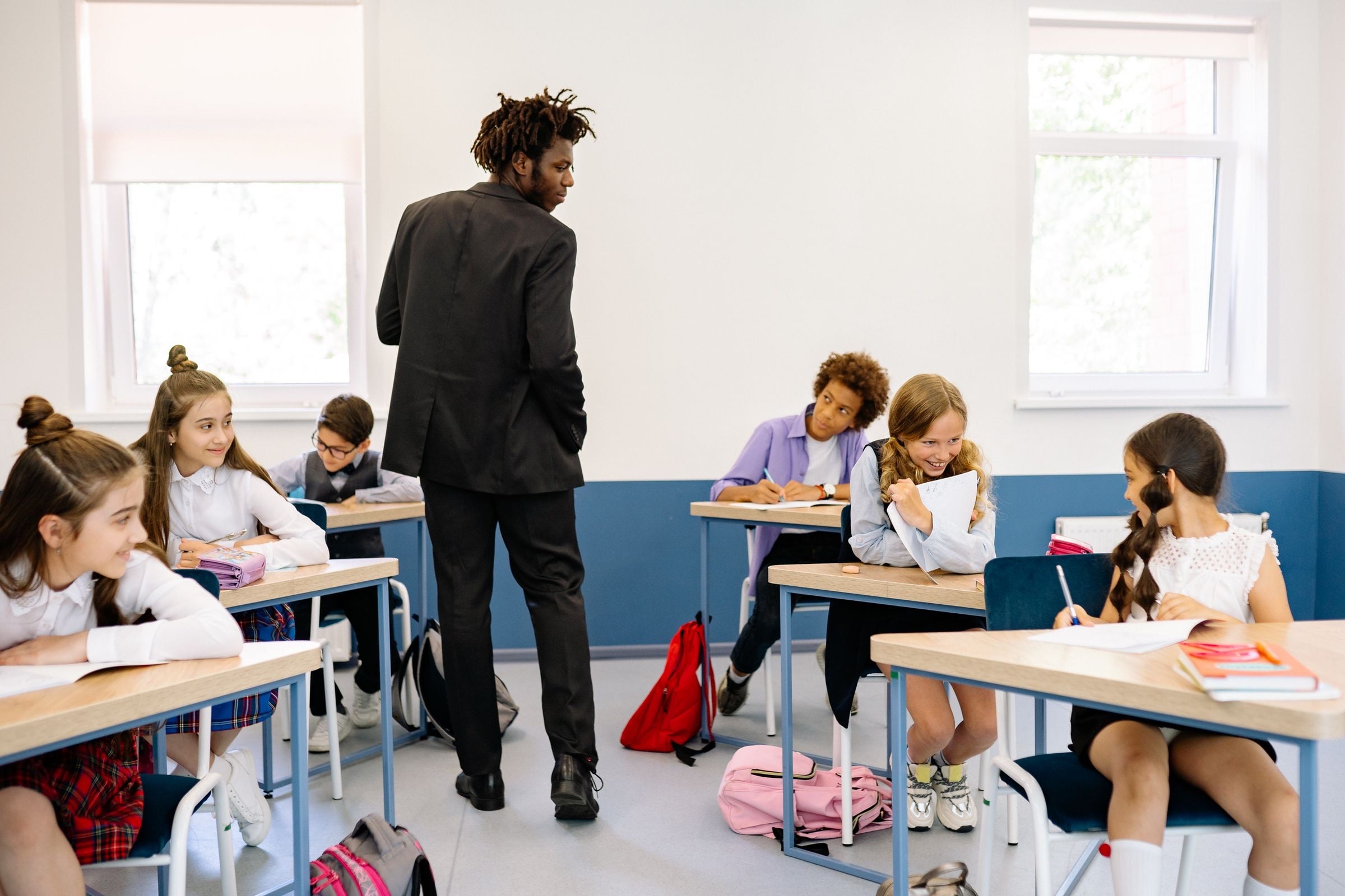 A teacher walking between rows of pupils in school uniform working at their desks