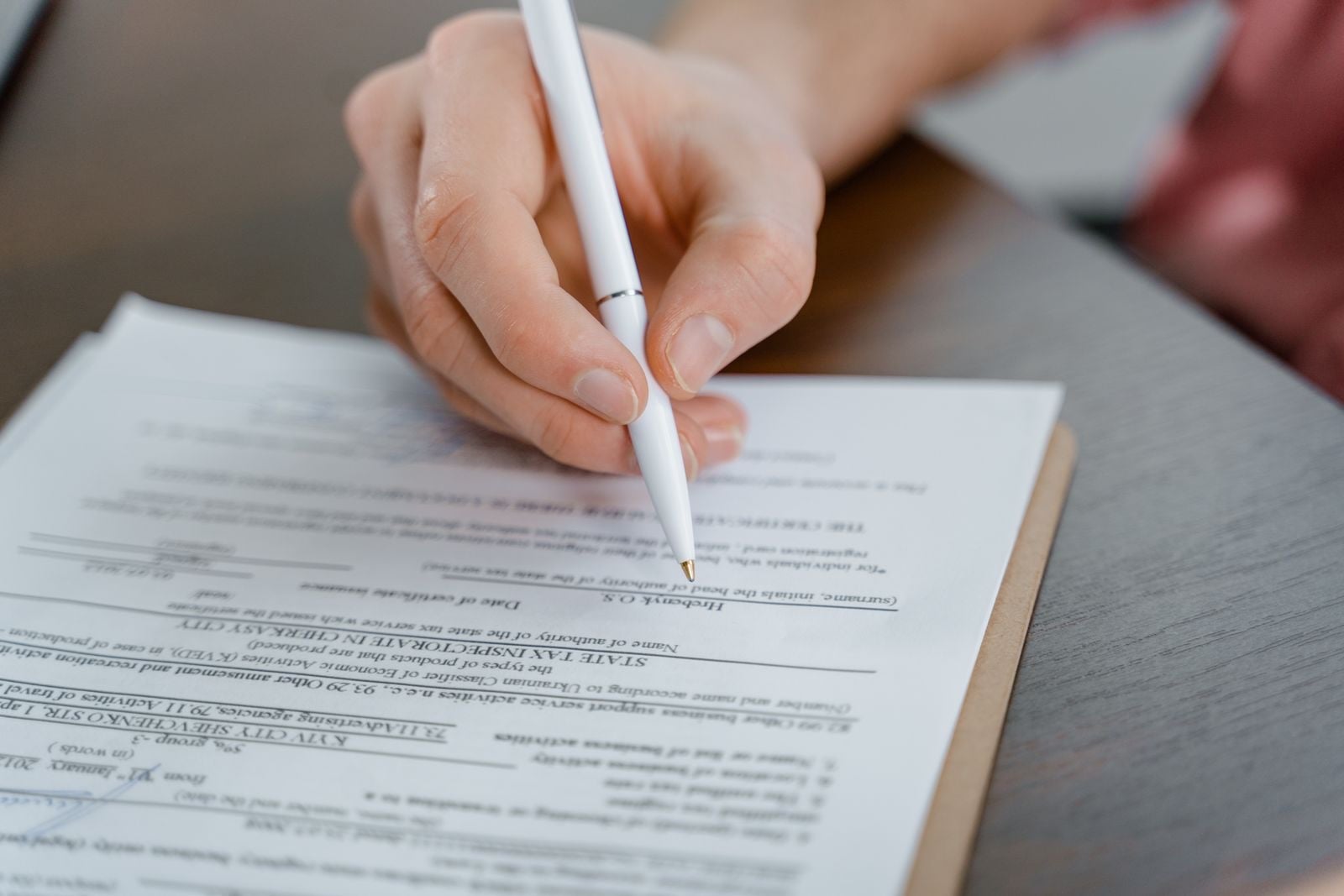 A hand holding a white pen, signing a printed form on a desk
