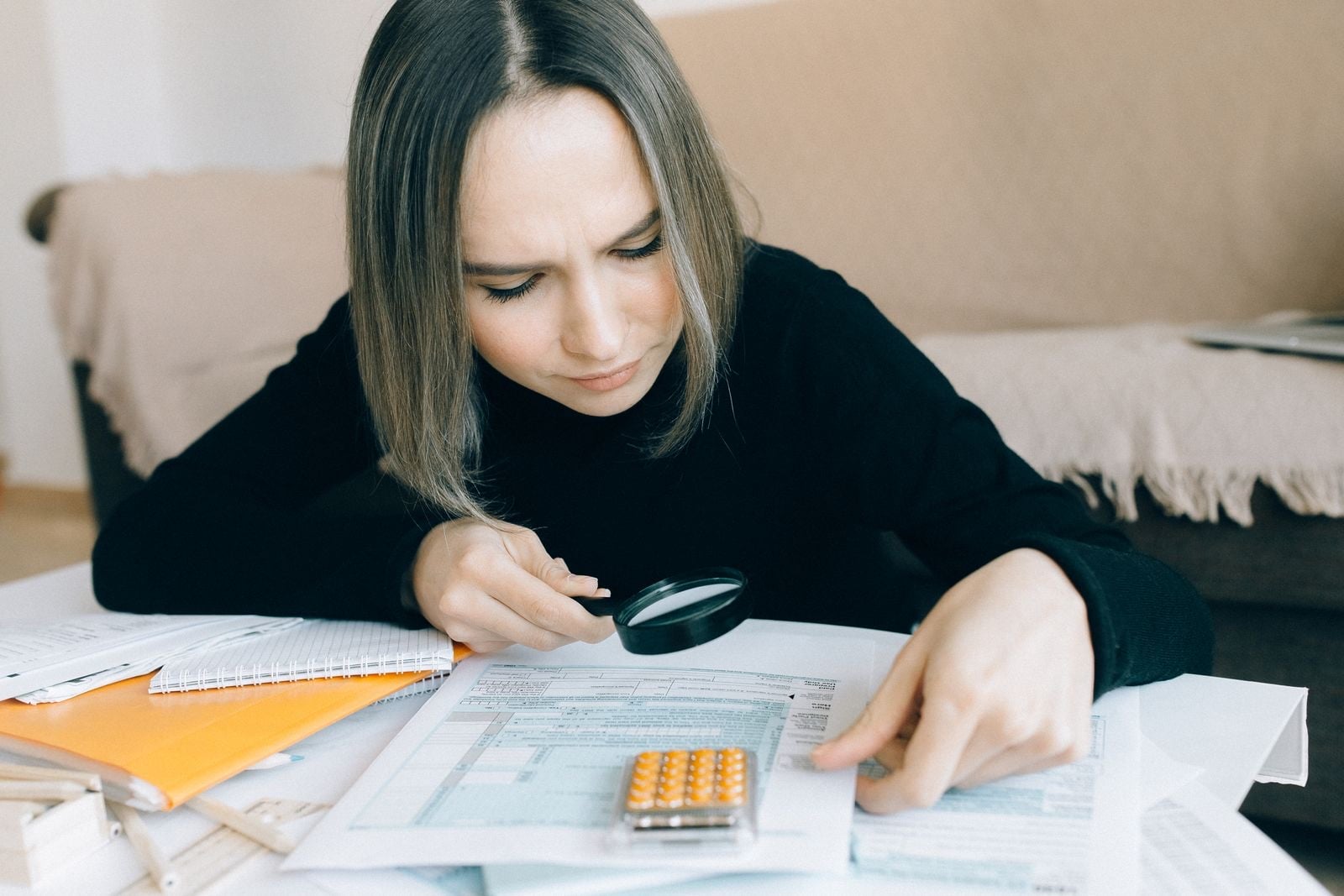 A woman in a black jumper studying a printed form through a magnifying glass