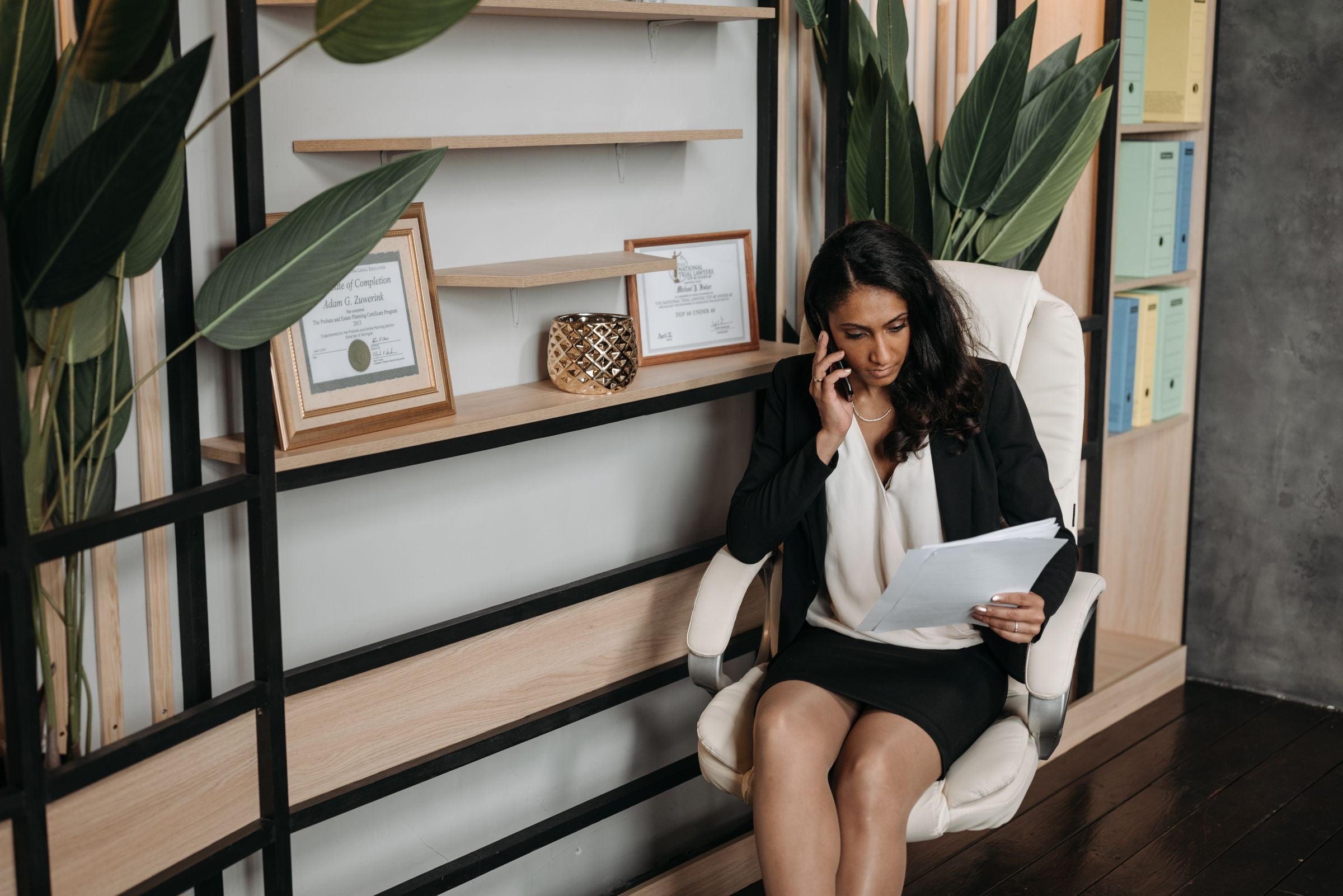 A compliance officer on the phone reading through a printed document in her office
