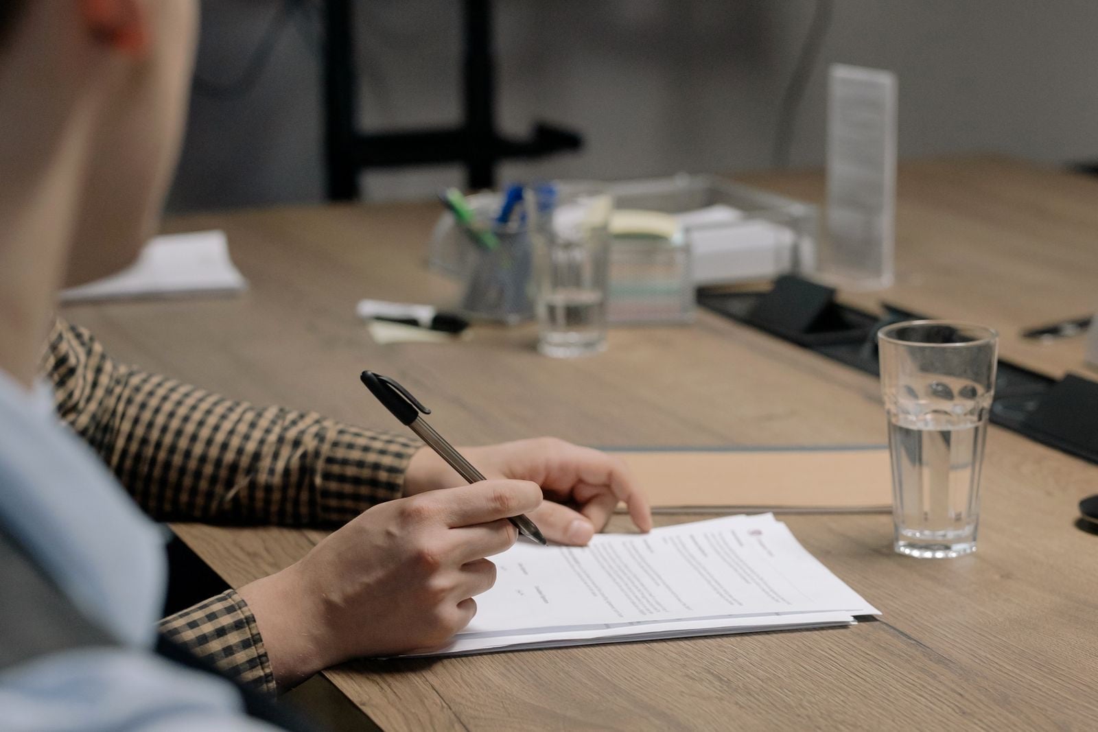 A person filling in a printed form with a pen at an office table