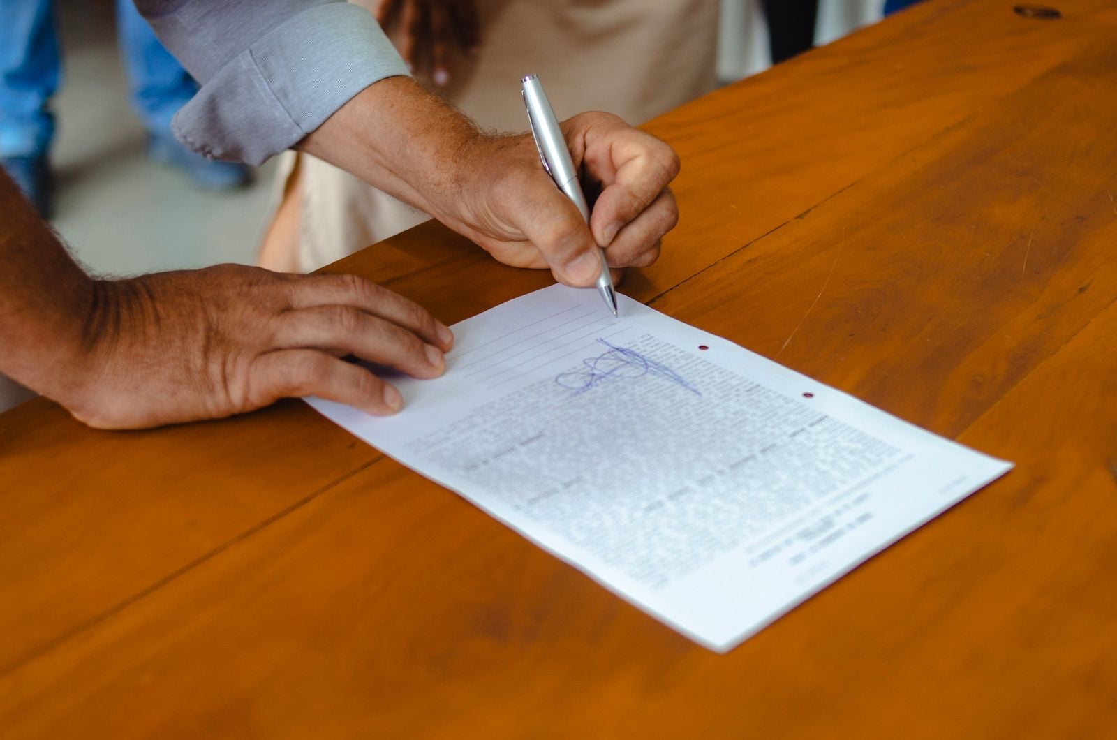 A hand signing a printed agreement on a wooden table
