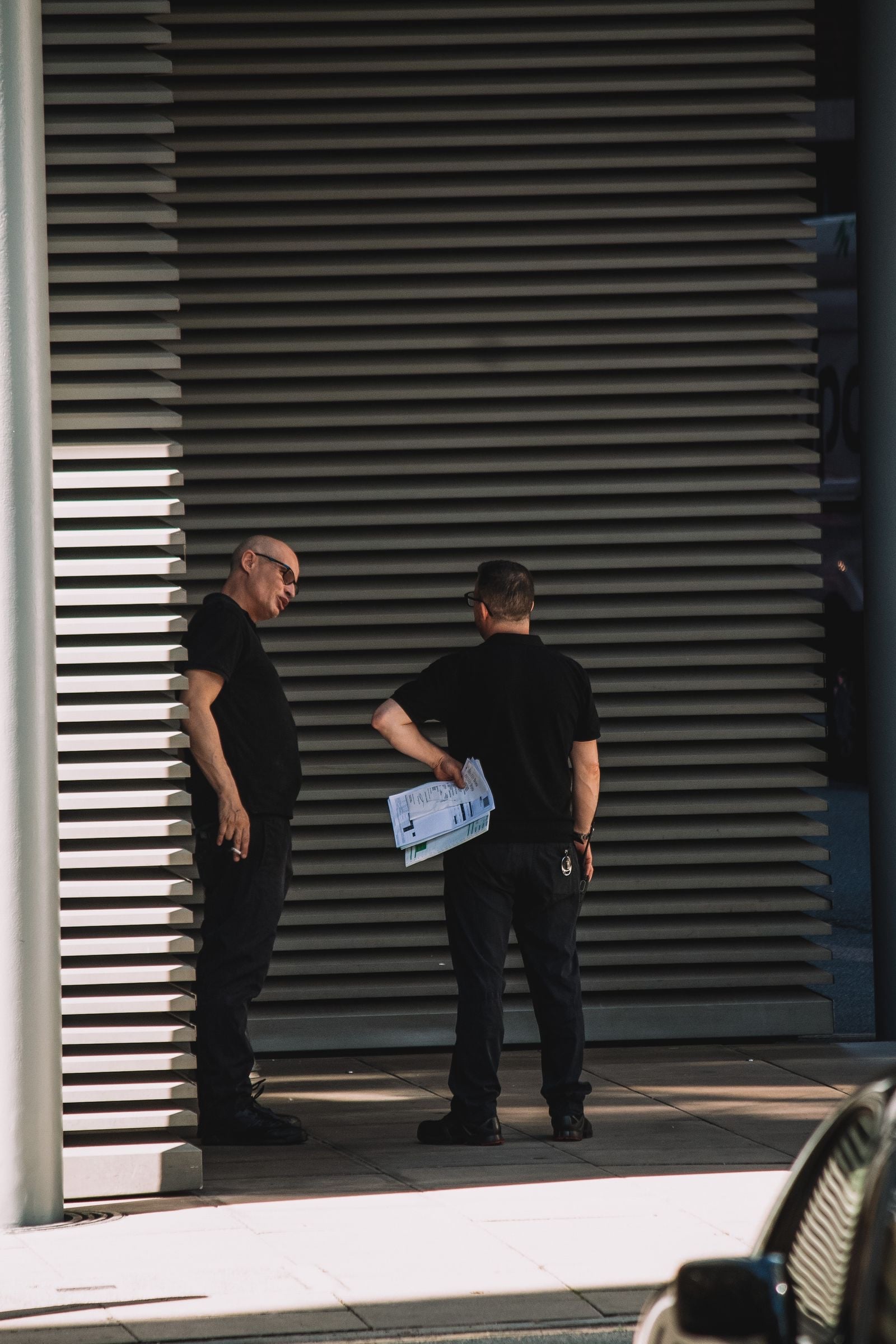 Two security officers in black uniforms talking outside a shuttered entrance in London, one holding papers