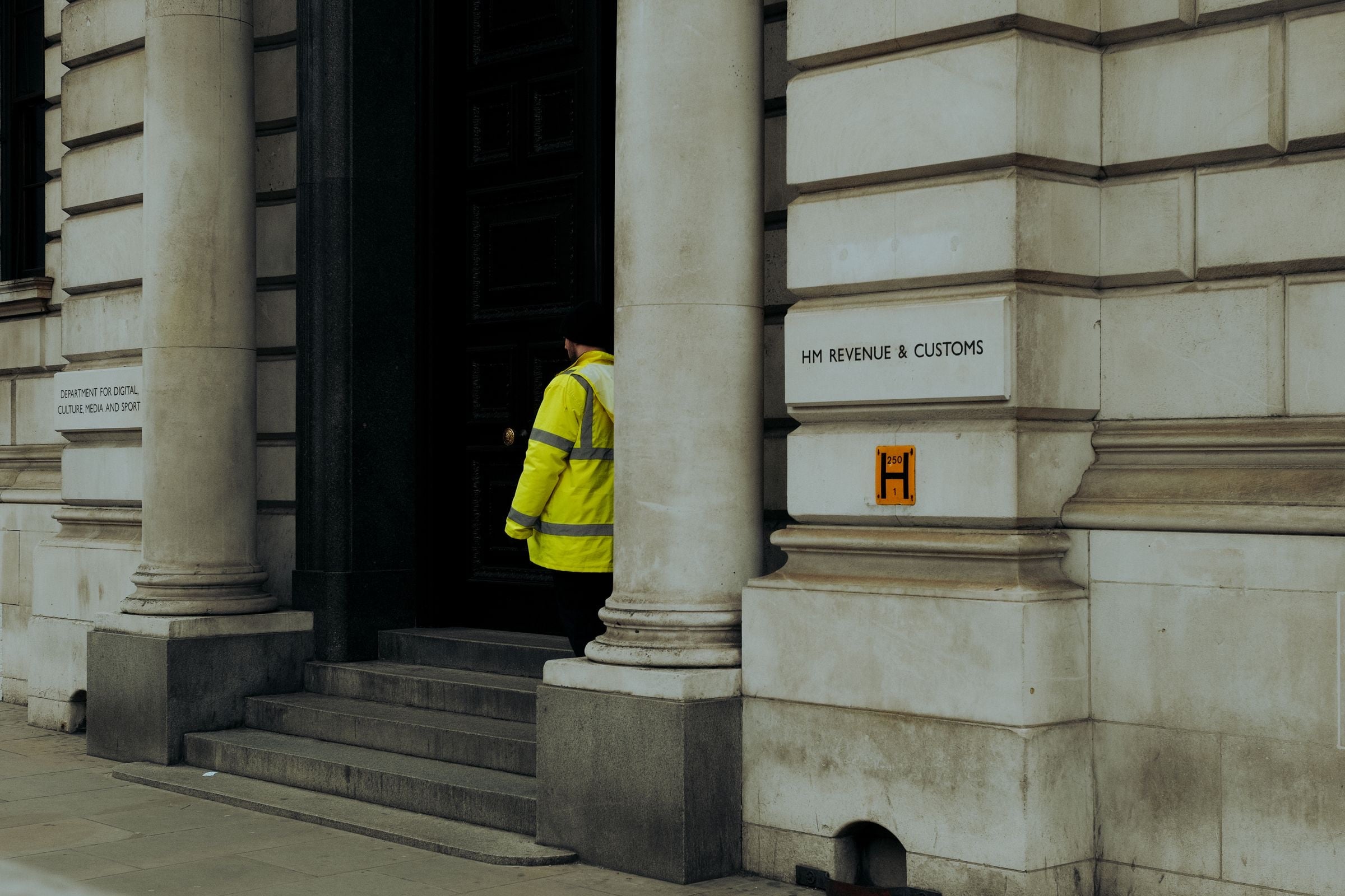 A security officer in a yellow high-visibility jacket at the stone doorway of a government building in London