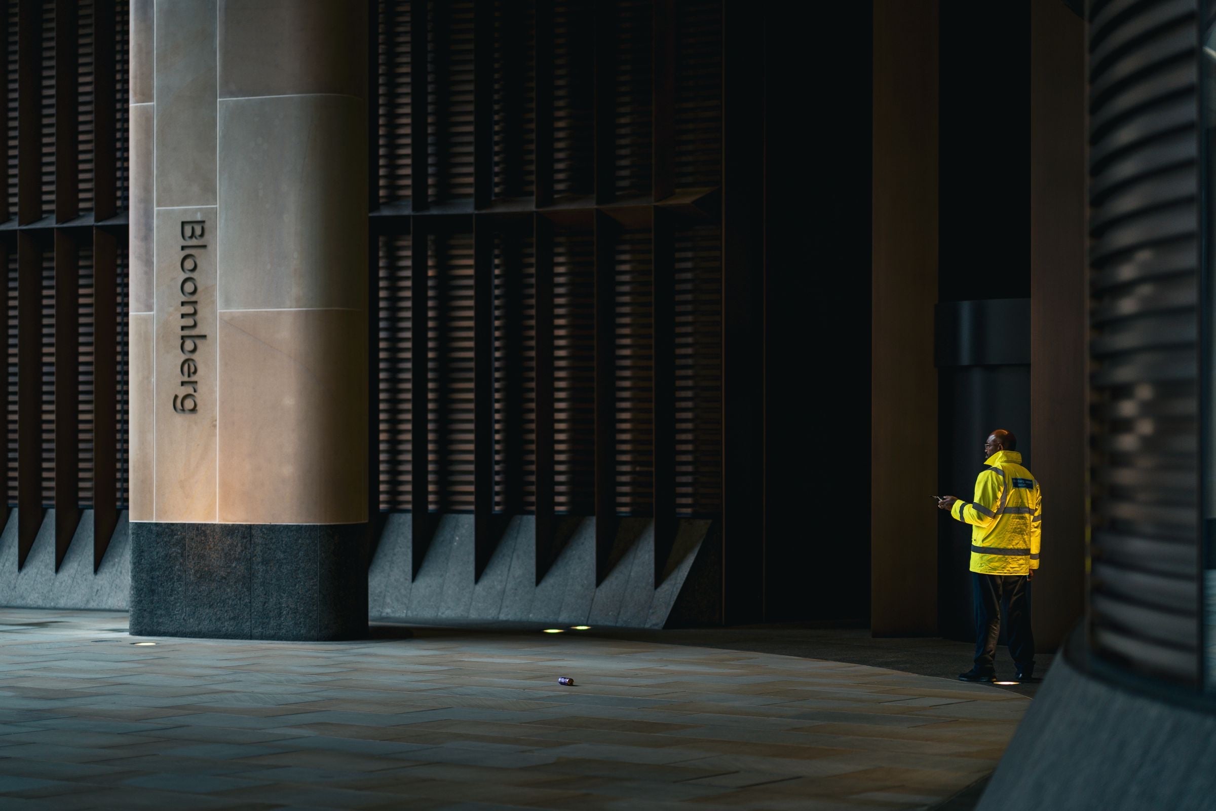 A lone security officer in a yellow high-visibility jacket at the entrance of a London office building at night