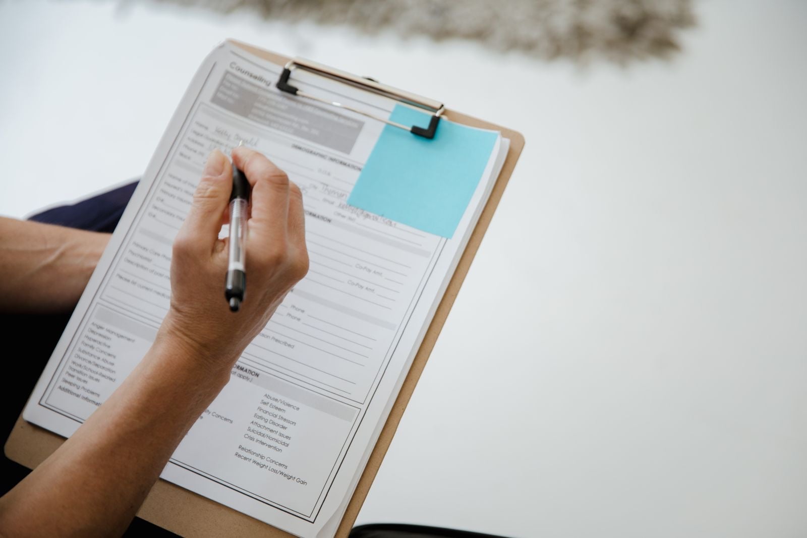 A hand filling in a printed form on a clipboard with a ballpoint pen