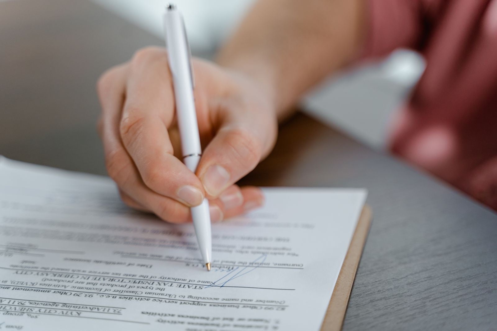 A hand filling in a printed form with a white ballpoint pen