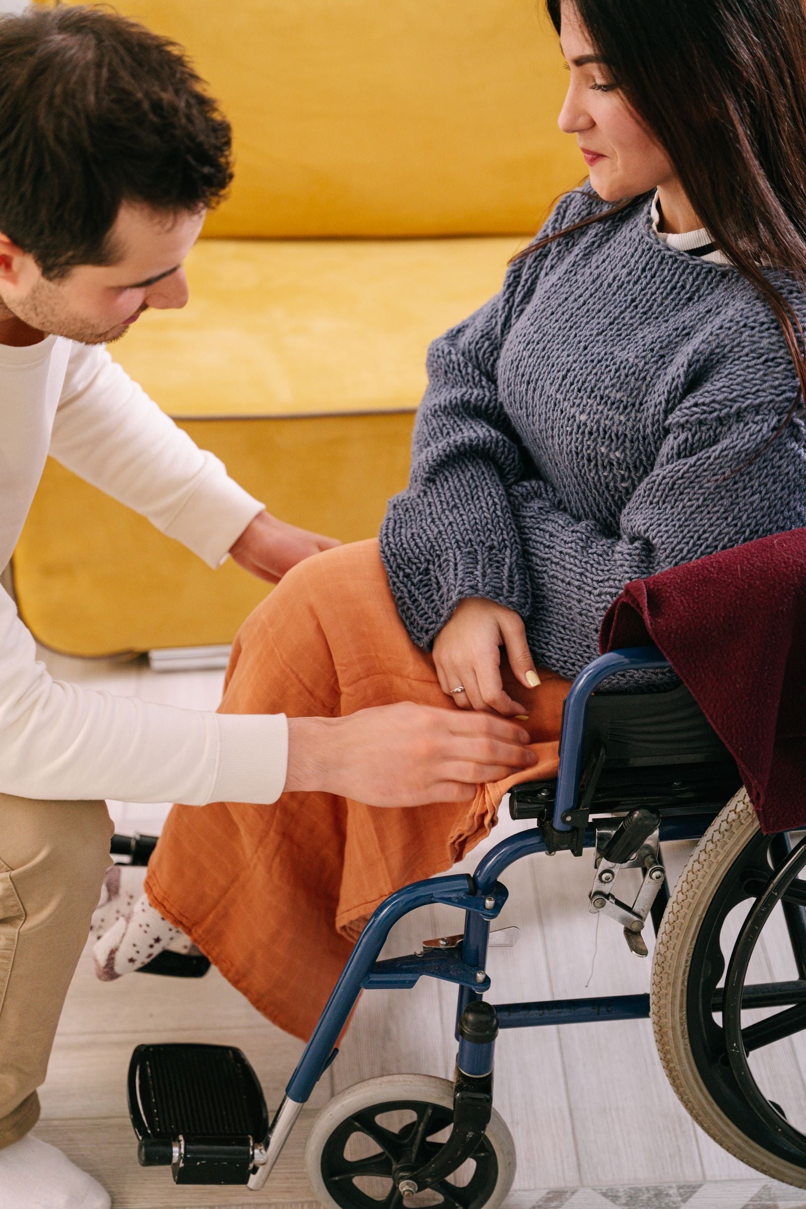 A young man kneeling to settle a woman’s feet on the footrests of her wheelchair
