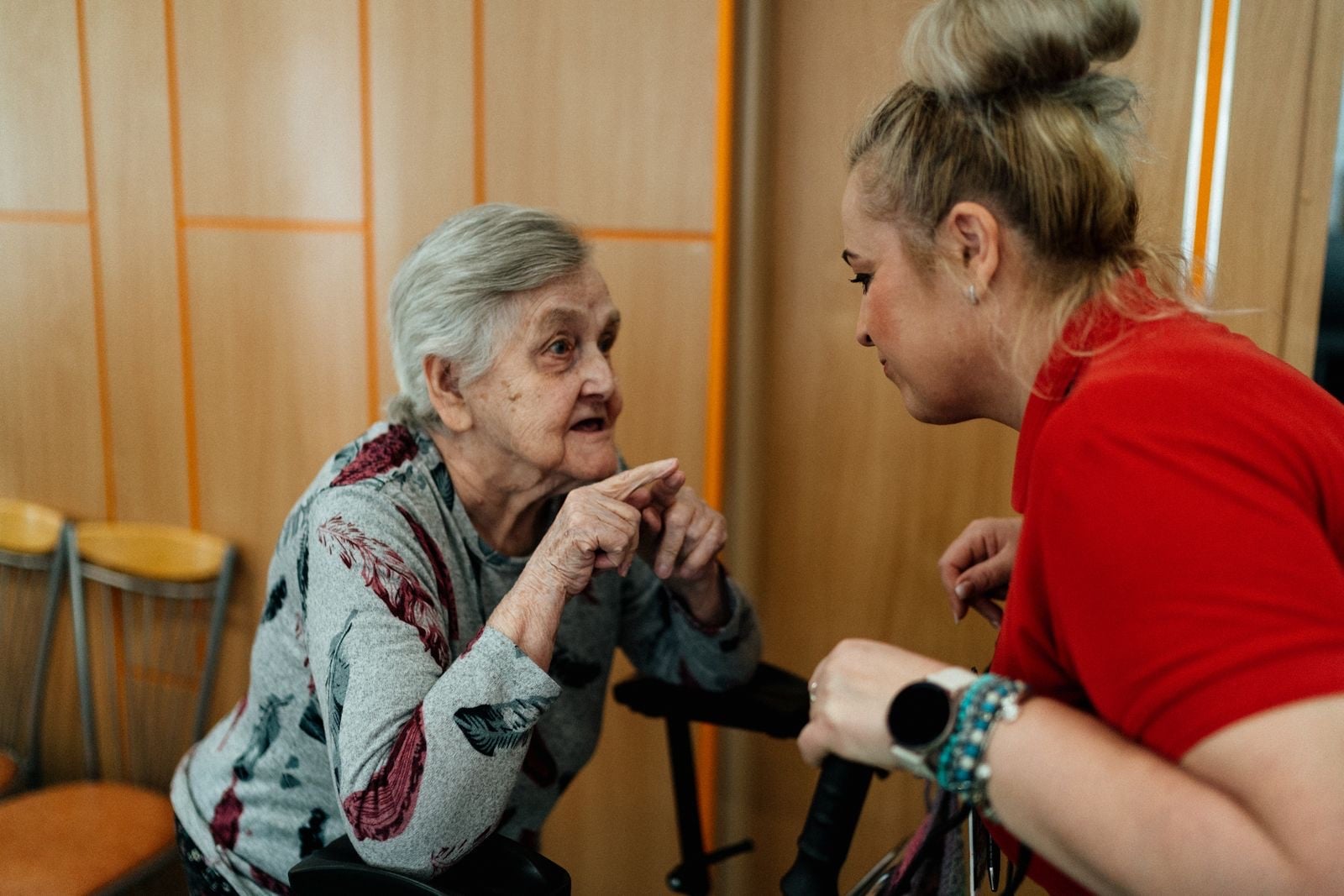 A care worker in a red top crouching to talk face to face with an older woman